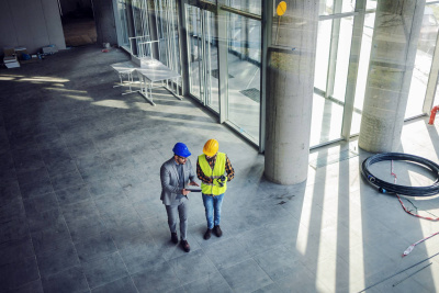 Zwei Bauarbeiter mit Helmen und Tablet auf der Baustelle