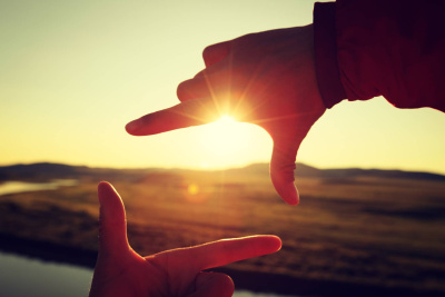 Menschliche Hände, die einen Rahmen über den Sonnenuntergang machen