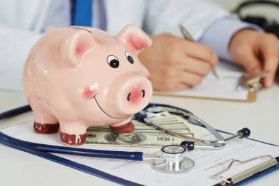 Sparschwein steht auf einem Bürotisch mit Klemmbrett, Stetoskop und Dollarscheinen.