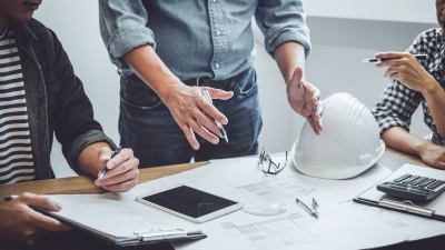 Ingenieure und Architekten besprechen Pläne, die auf einem Tisch mit Bauhelm liegen.