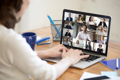 Person arbeitet am Notebook und sieht auf dem Bildschirm andere Personen in einem Online-Meeting.
