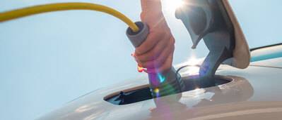 Eine Hand steckt ein Ladekabel in die Buchse eines Elektroautos